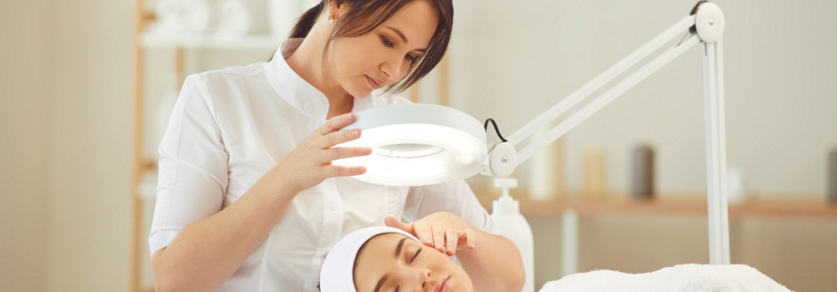 Spa professional using a magnifying lamp to assess a client’s face during a skincare treatment.