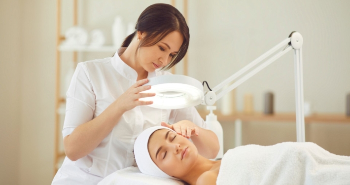 Spa professional using a magnifying lamp to assess a client’s face during a skincare treatment.