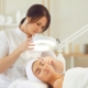 Spa professional using a magnifying lamp to assess a client’s face during a skincare treatment.